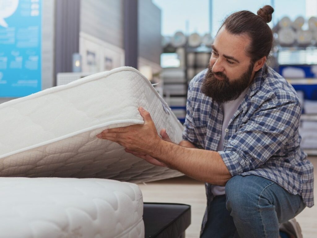 Man with beard is putting mattress in place