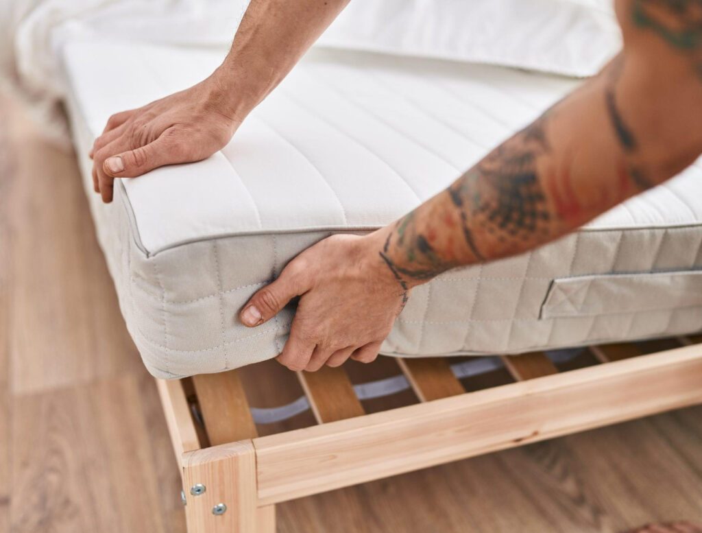 Man is putting mattress on the bed